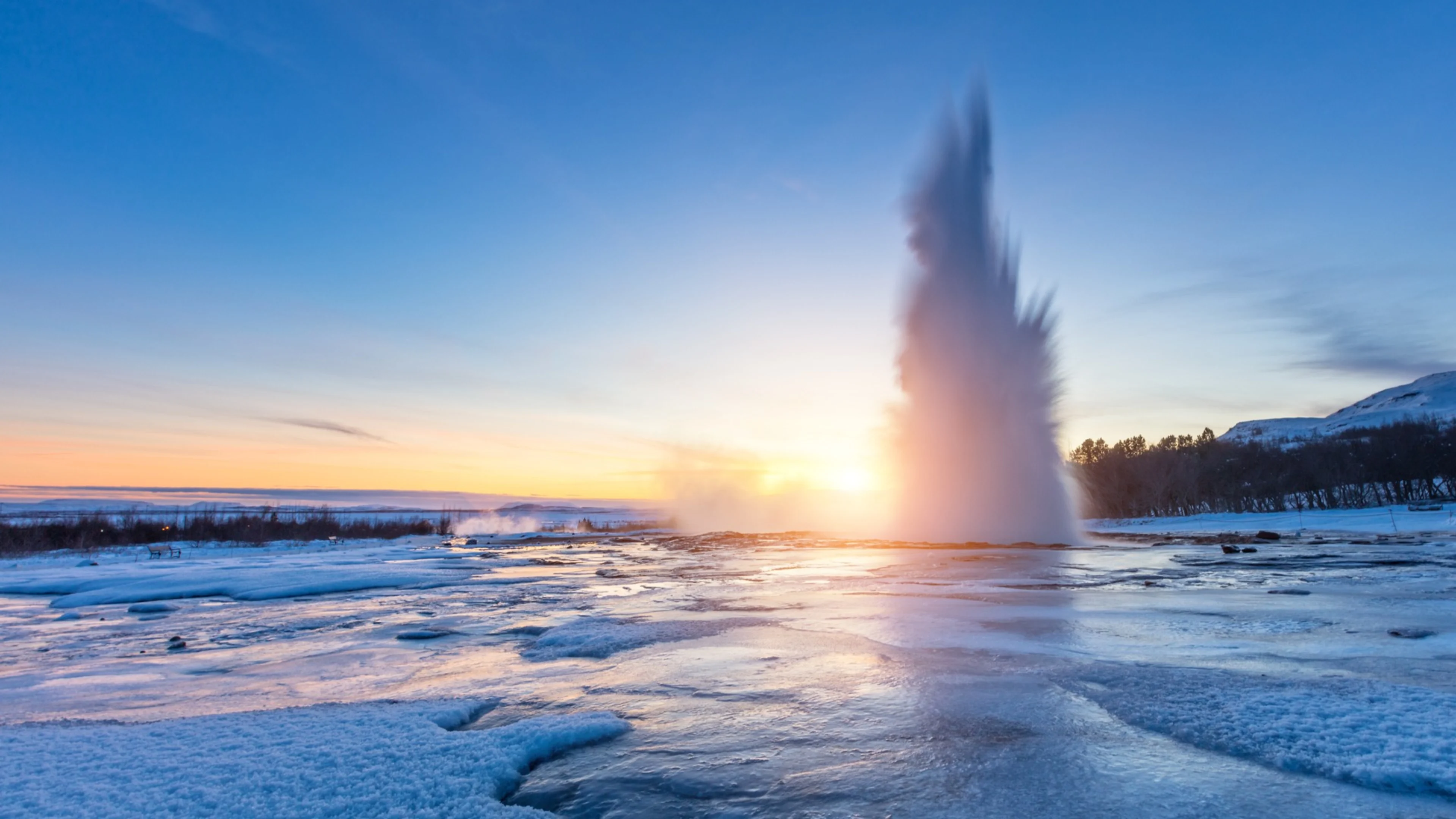 The Strokkur geyser erupting at sunset above frozen ground